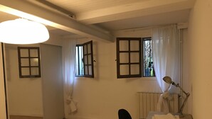 Una habitación con escritorio, silla, radiador y dos ventanas con cortinas.