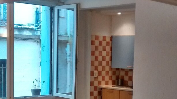 Una habitación amplia con un gran ventanal, una silla de madera y una zona de cocina con un salpicadero a cuadros.