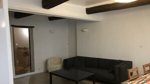 Una sala de estar con un sofá oscuro, una mesita pequeña y una mesa de comedor de madera con mantel colorido.