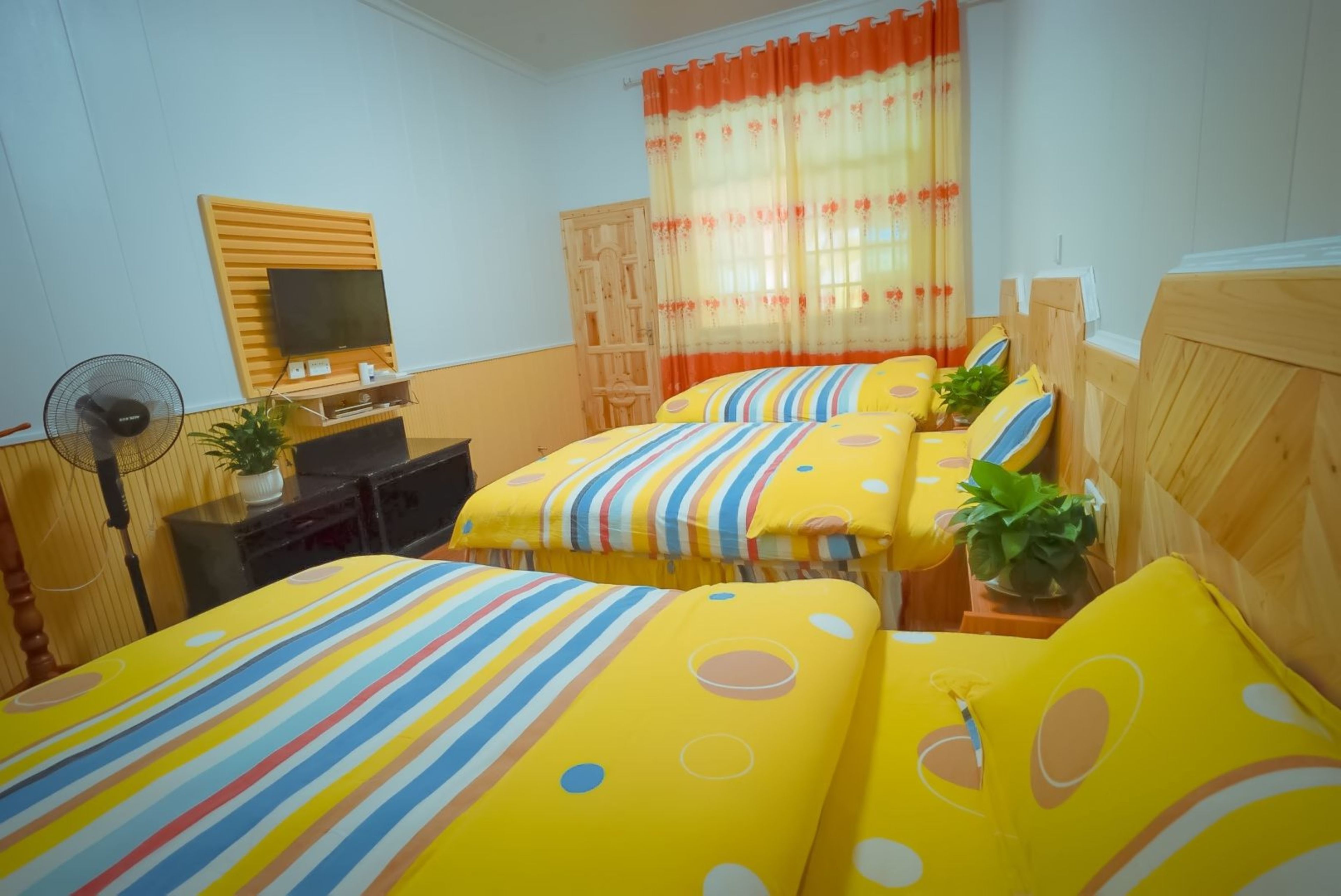 A hotel room with two beds, a TV on a wooden stand, a desk with a fan, and a window with curtains.