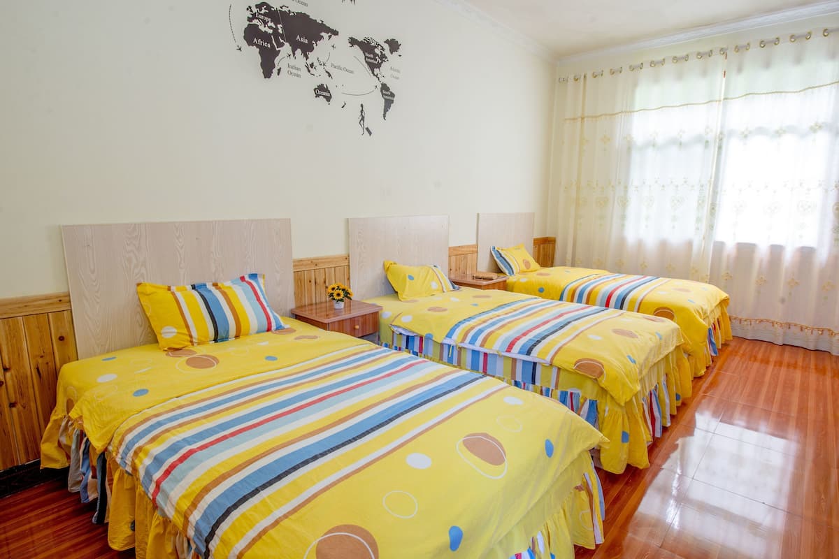 A hotel room with three beds, each with a yellow bedspread and striped pillows. There is a world map on the wall and a window with curtains.