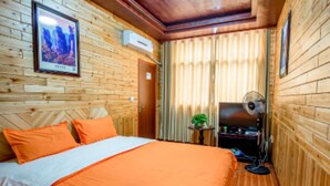 Una habitación con paneles de madera, una cama, un ventilador y una mesita con una planta.