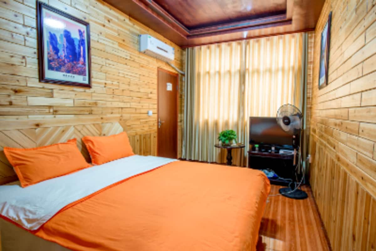 A wooden-paneled room with a bed, a fan, and a small table with a plant.