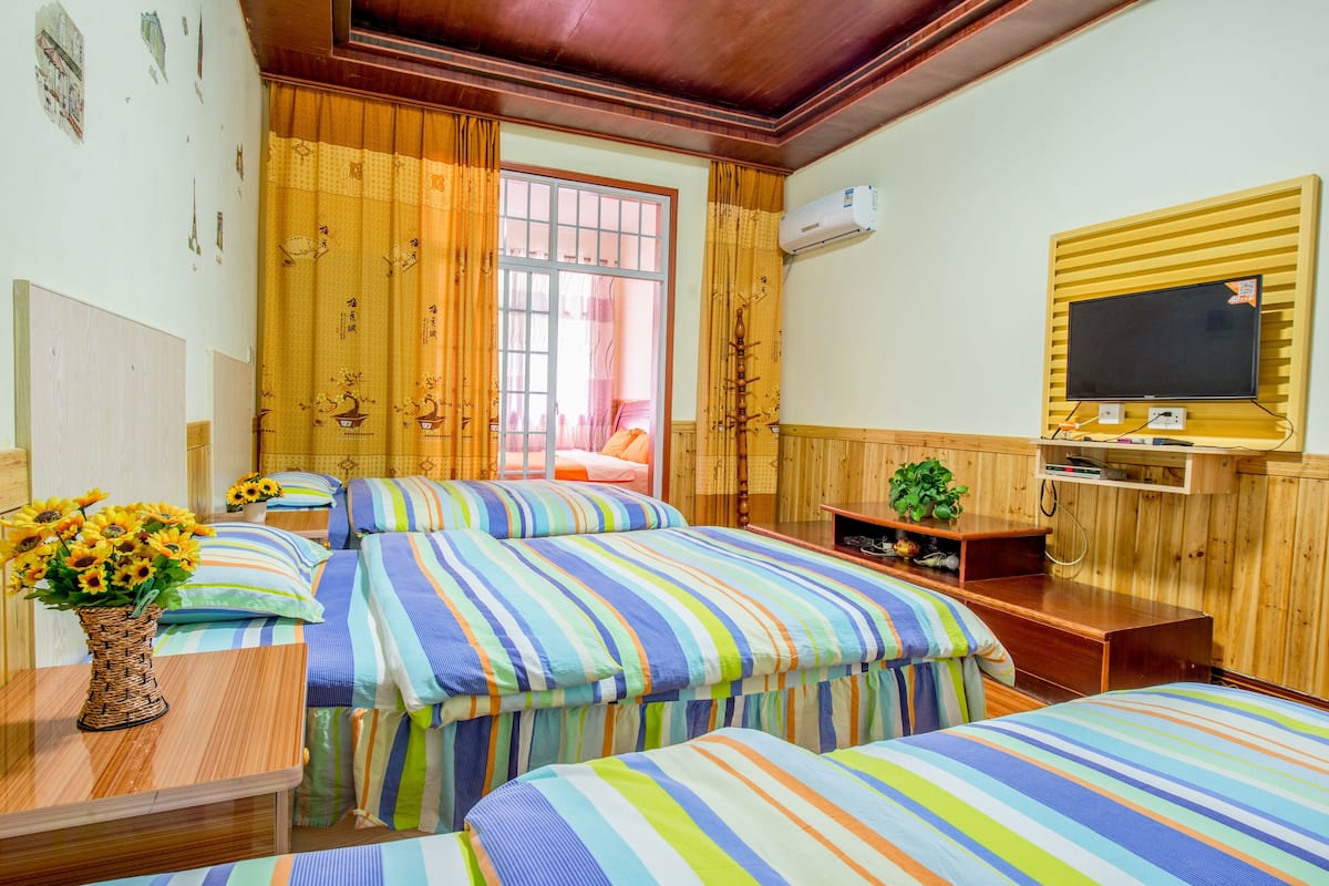A hotel room with three beds, a TV, and a wooden wall.