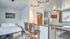Une chambre d’hôtel moderne, équipée d’un lit, de deux chaises en bois, d’un petit comptoir et d’œuvres d’art accrochées aux murs.