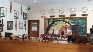 A reception desk with clocks, framed artwork, and a mural depicting a traditional scene. - Law Ka Thit Sar Hotel - Hostel (Nyaung-U)