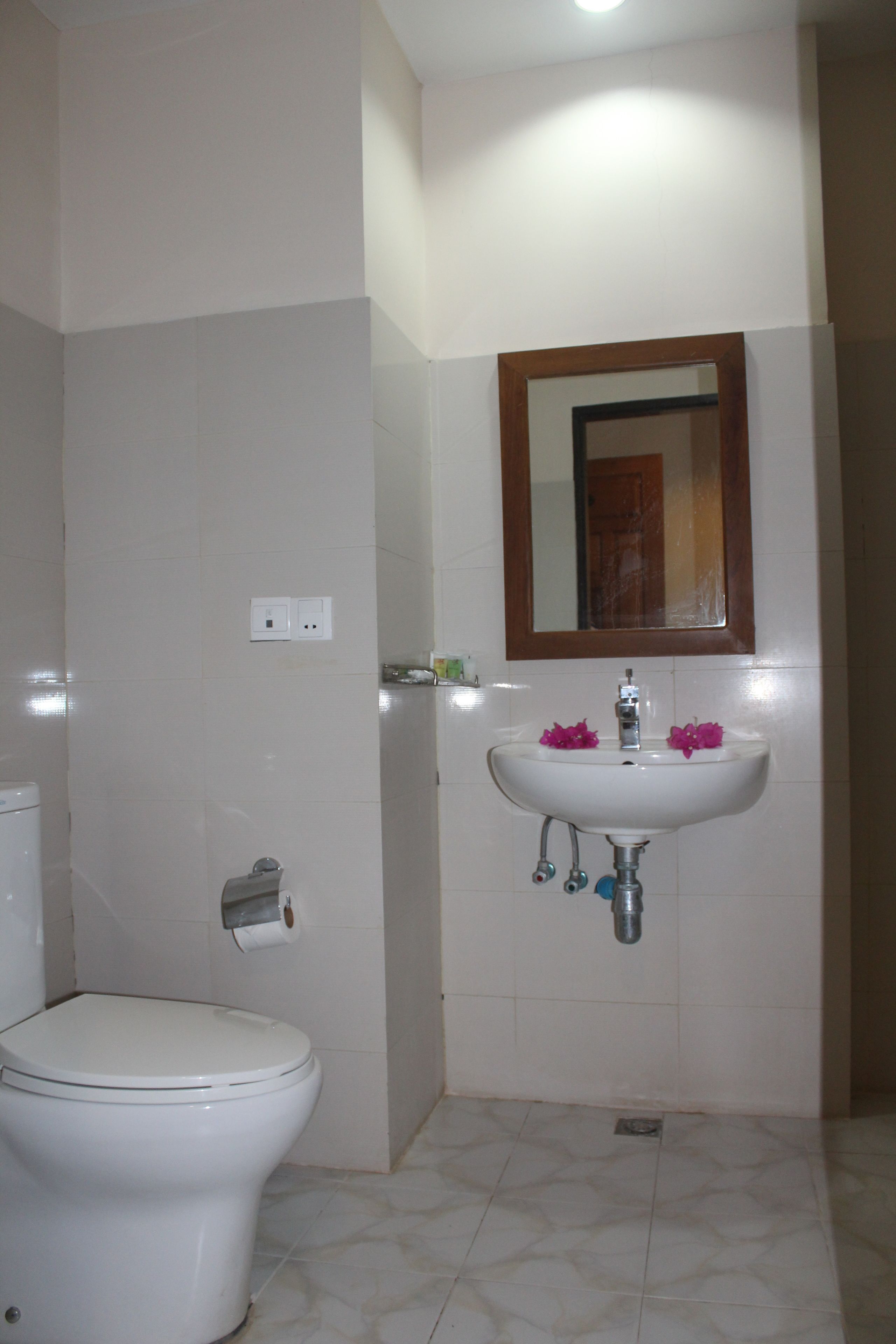 A bathroom with a toilet, a sink with a mirror above it, and a roll of toilet paper on the wall.
