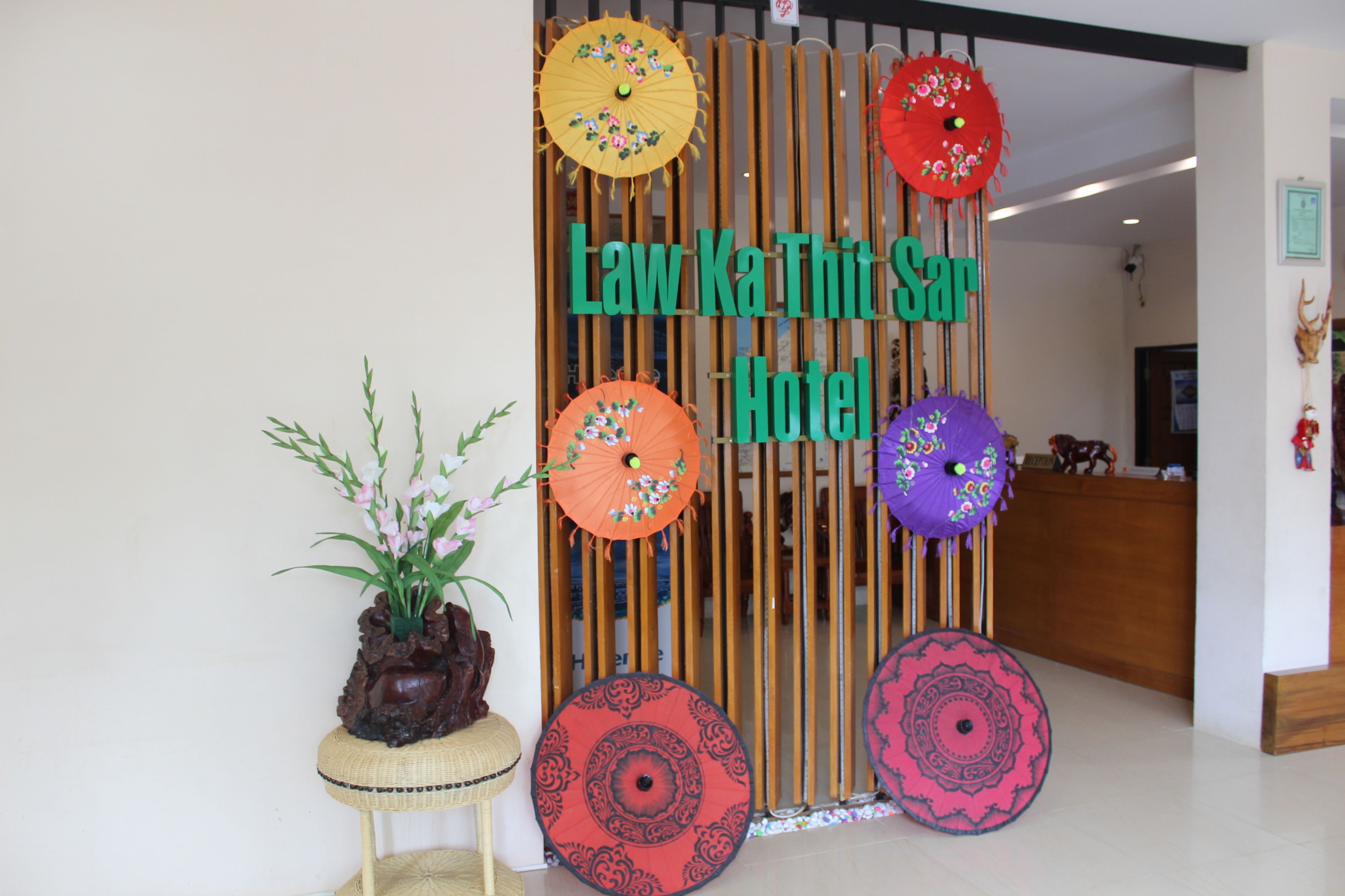 Zona de recepción con un panel de madera que muestra el nombre 'Law Ka Thi Sar Hotel'.