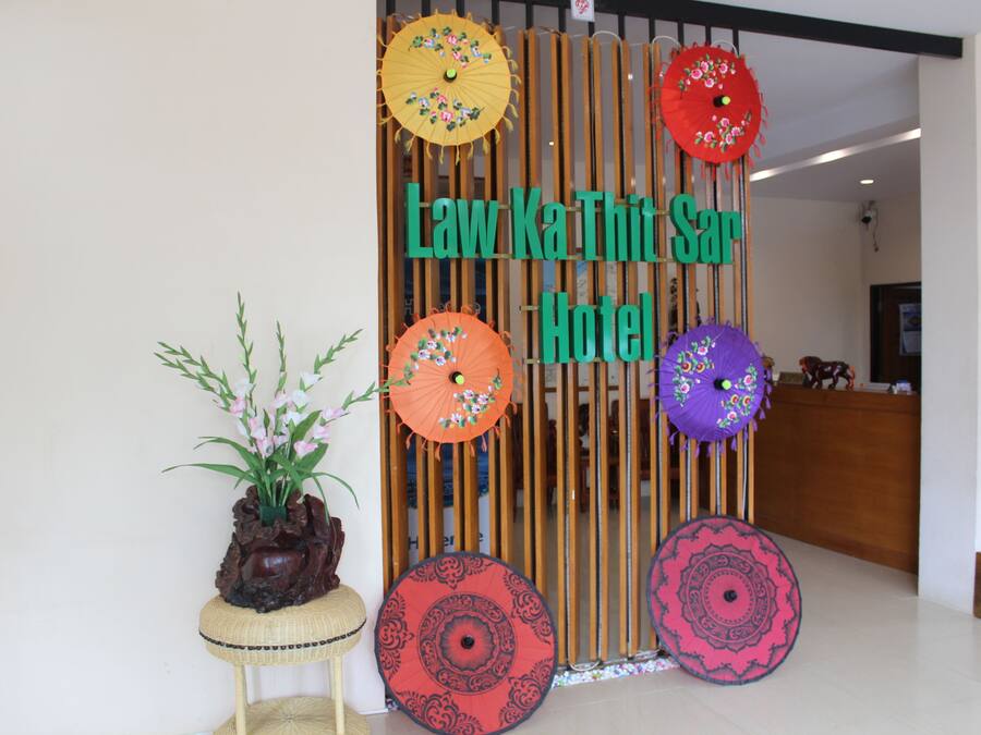 Uma área de recepção com um painel de madeira exibindo o nome 'Law Ka Thi Sar Hotel'.