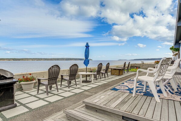 A deck with outdoor seating, a grill, and a view of the water. - Beachfront Whidbey Island Home + Apartment! (Langley)