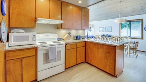 A kitchen with wooden cabinets, a white stove, and a microwave. There is a dining area with a table and chairs. - Beachfront Whidbey Island Home + Apartment! (Langley)