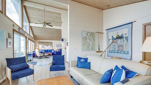 A spacious living room with a high ceiling, large windows, and a view of the outdoors. There are multiple seating areas with blue and white furniture. - Beachfront Whidbey Island Home + Apartment! (Langley)