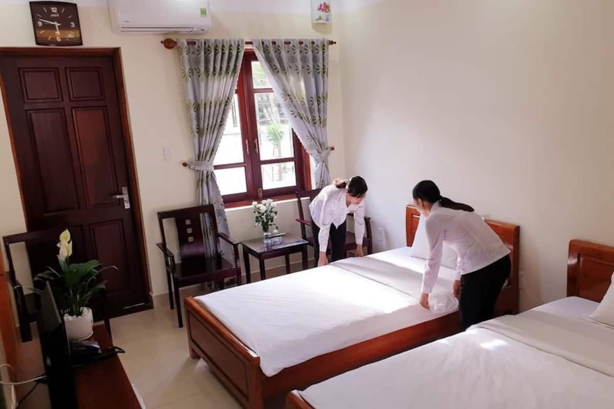 A hotel room with two beds, a desk, a chair, and a window with curtains.