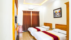 A hotel room with two beds, a wooden headboard, a bedside table, a wall-mounted air conditioner, a framed picture, and a curtain. - Bo Xay Dung Vung Tau (Ho Chi Minh City)