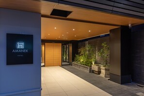 A modern hotel entrance with a sign reading "AMANEK HOTEL," a wooden ceiling, recessed lighting, and a planter with greenery. - HOTEL AMANEK Kyoto Kawaramachi Gojo (Kyoto)