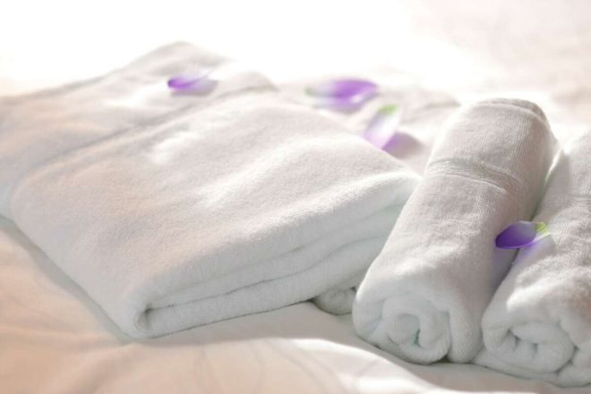 Neatly folded white towels with purple ribbons on a bed.