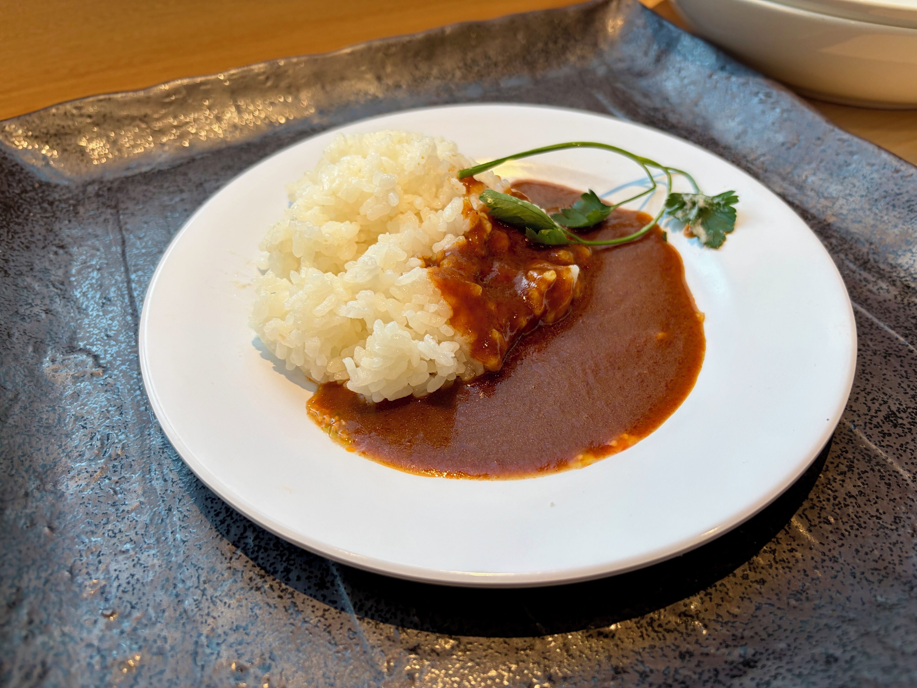 Un plato de arroz blanco con salsa marrón y una guarnición sobre una superficie azul texturizada.
