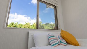 Una camera da letto con un letto, cuscini e una finestra con vista su piante.
