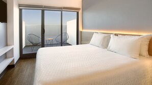 A hotel room with a large bed, a sliding glass door to a balcony, a small table, and a chair. - Gamma Querétaro (Querétaro)