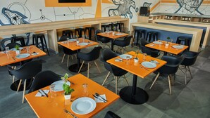 A restaurant interior with orange tables and black chairs, featuring a modern design with geometric wall art. - Gamma Querétaro (Querétaro)