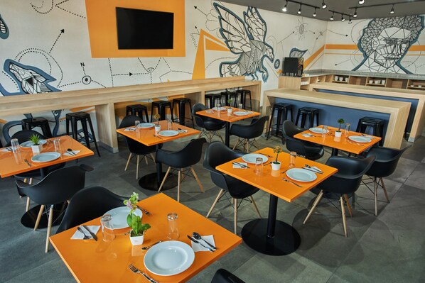 A restaurant interior with orange tables and black chairs, featuring a modern design with geometric wall art. - Gamma Querétaro (Querétaro)