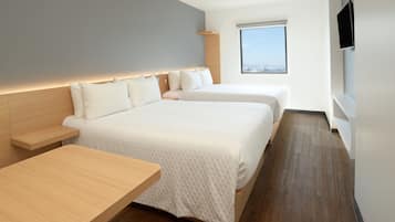 Una habitación de hotel moderna con dos camas, una mesita de noche de madera, un televisor de pantalla plana y un ventanal con vista a la ciudad.