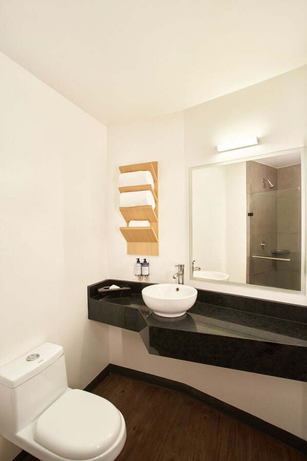 Un baño moderno con inodoro blanco, lavabo negro y un espejo grande sobre el lavabo.