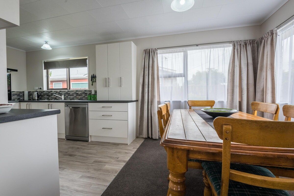 A modern kitchen with white cabinets, a stainless steel dishwasher, and a dining area with a wooden table and chairs.