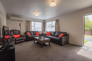 A living room with two leather sofas, a coffee table, and a television. - Beez Kneez - Central, Spa Pool, Sleeps 6 (Rotorua Township)