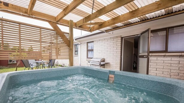 Une piscine extérieure couverte, surmontée d’une pergola en bois, avec un barbecue et un bâtiment en briques en arrière-plan.