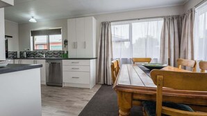 Une cuisine moderne avec des meubles blancs, un lave-vaisselle et un coin repas comprenant une table et des chaises en bois.