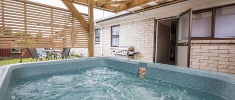A swimming pool with a wooden pergola overhead, a barbecue area, and a brick house in the background.