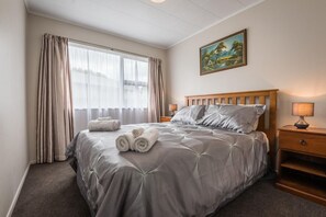A hotel room with a bed, a nightstand, a lamp, and a painting on the wall.