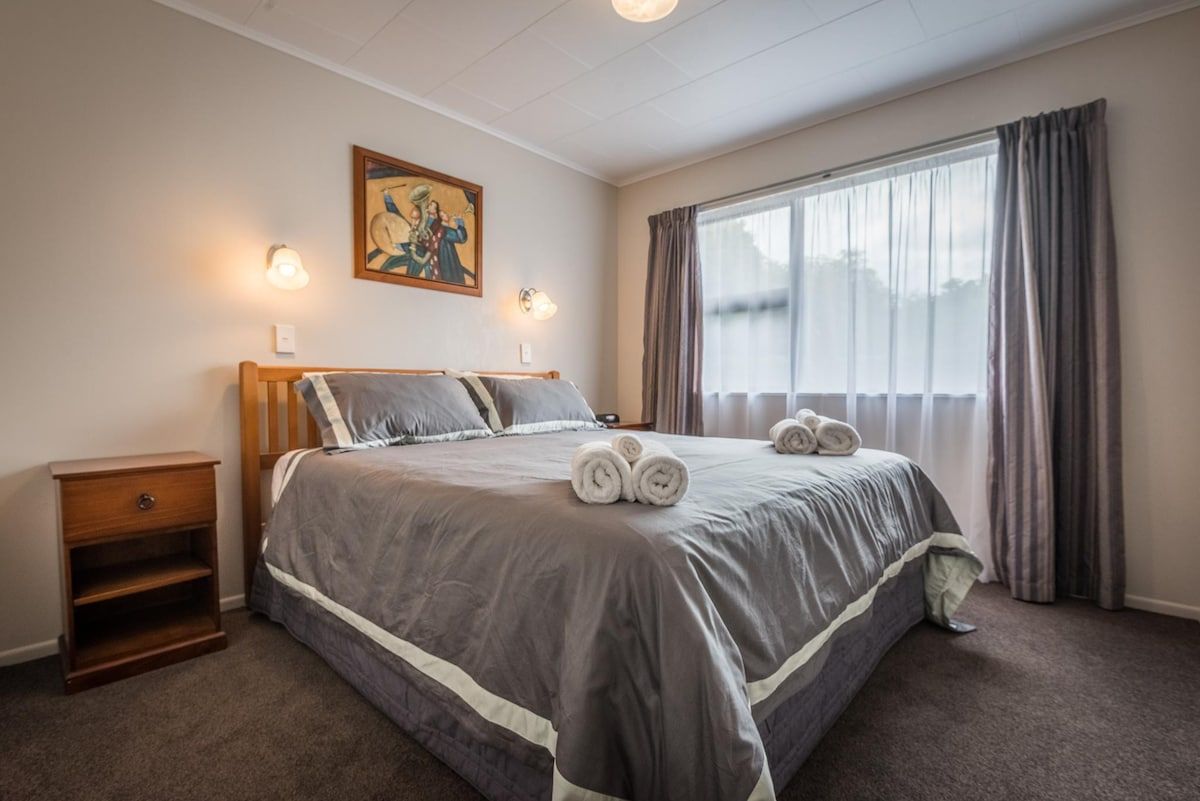 Une chambre d’hôtel avec un grand lit, deux tables de chevet, un tableau au mur et une fenêtre avec des rideaux.