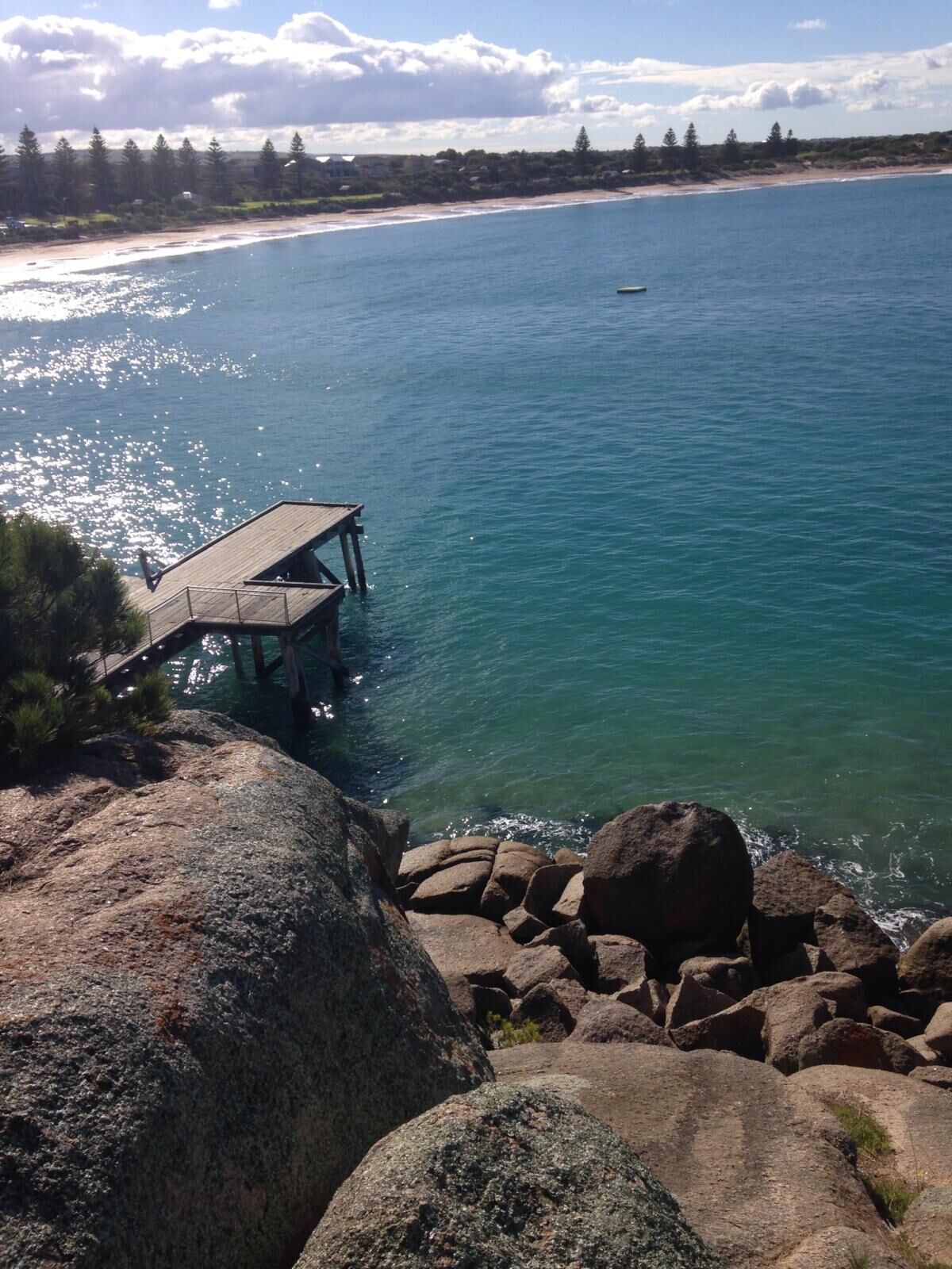 A wooden pier extending into a calm body of water, surrounded by large rocks and trees.