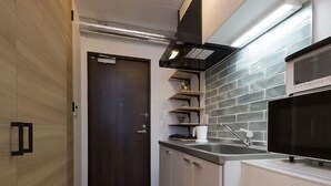 A narrow kitchen with a dark wooden door, white cabinets, a stainless steel sink, and a microwave. - C3 Maison Philippe Shitaya 303 (Tokyo)