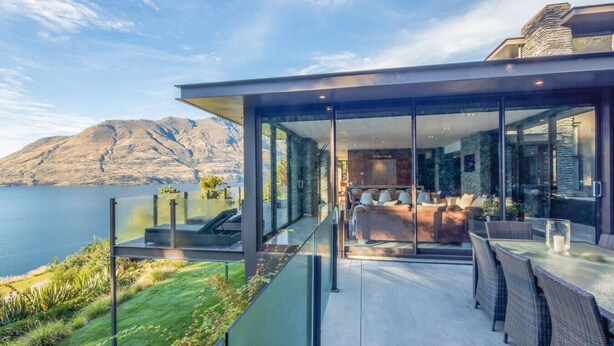A modern house with a glass-enclosed patio overlooking a lake and mountains. - Bellbrae by MajorDomo | Stylish 5-Bedroom Villa with Sauna, Spa Pool & Sweeping Lake Wakatipu Views (Queenstown)