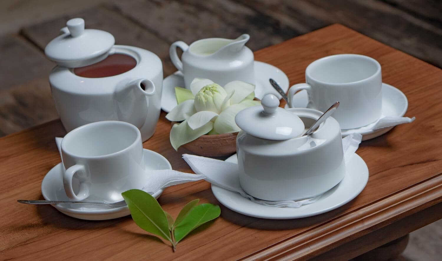 Ein Holztisch mit weißem Tee-Service, bestehend aus Teekanne, Tassen und Untertassen.