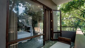 Een slaapkamer met een bed, een stoel en een balkon met uitzicht op bomen.