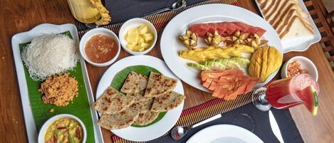 A table with various dishes including rice, curry, and grilled vegetables, along with a fruit salad and a drink.