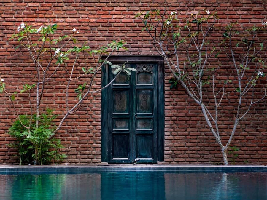 A brick wall with a dark wooden door and a pool in front.