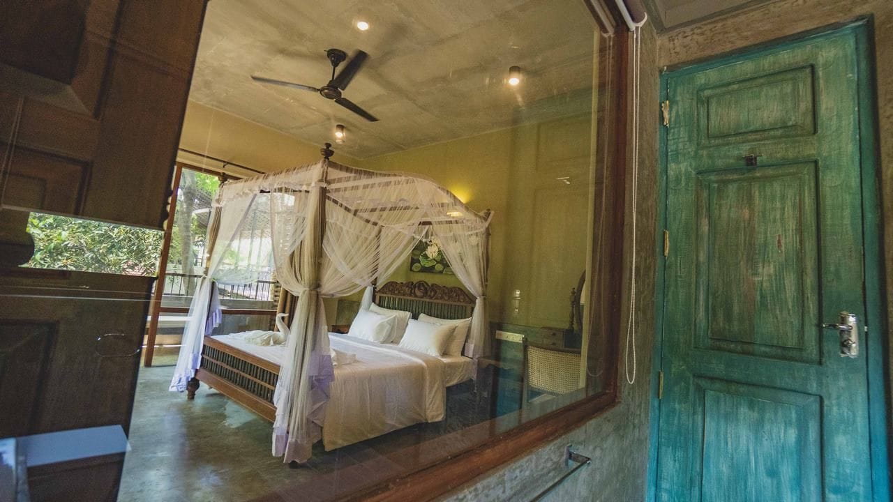 A room with a bed under a canopy, a green door, and a ceiling fan.