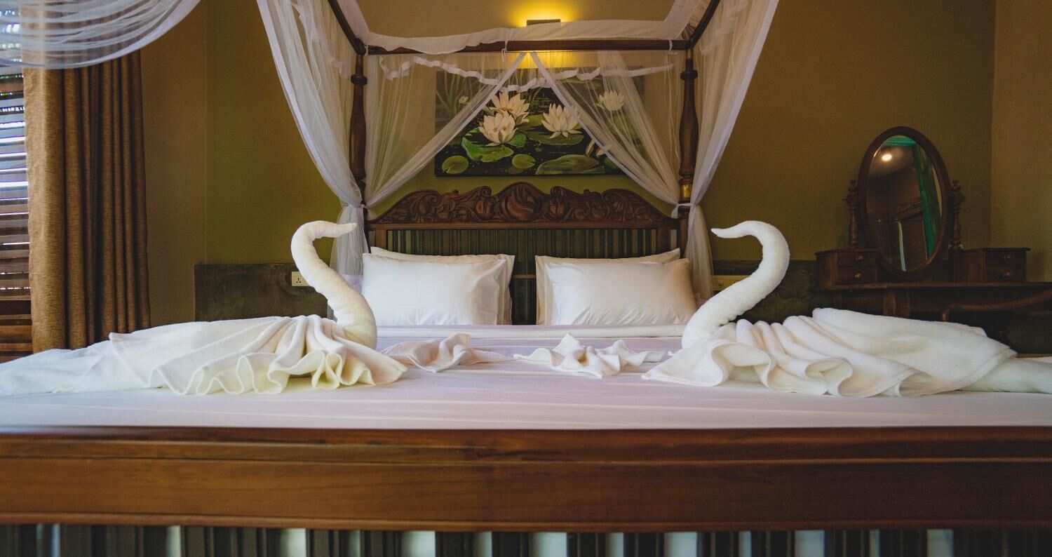 A bed with a canopy, swan-shaped pillows, and a painting of lotus flowers on the wall.