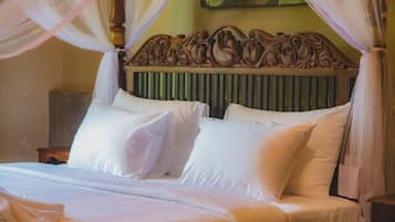 Een bed met witte lakens en een hemelbed, een houten hoofdbord met gedetailleerde houtsnijwerken en een groen gestreepte radiator achter het hoofdbord.