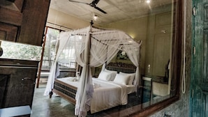 Een bed met hemelbed en witte lakens, een plafondventilator en uitzicht door een glazen deur.