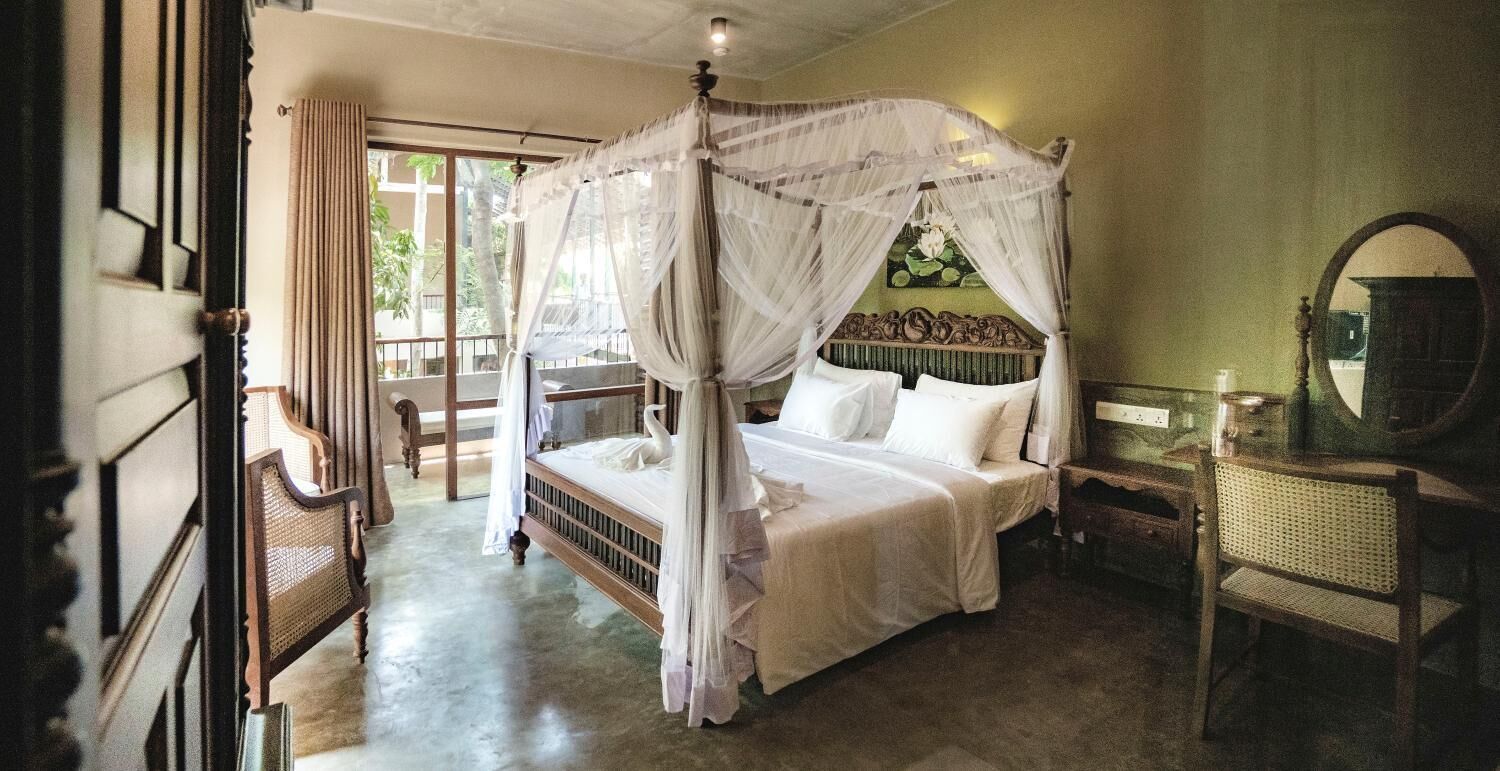 A four-poster canopy bed with white bedding, a wooden headboard, and a mirror on the wall.