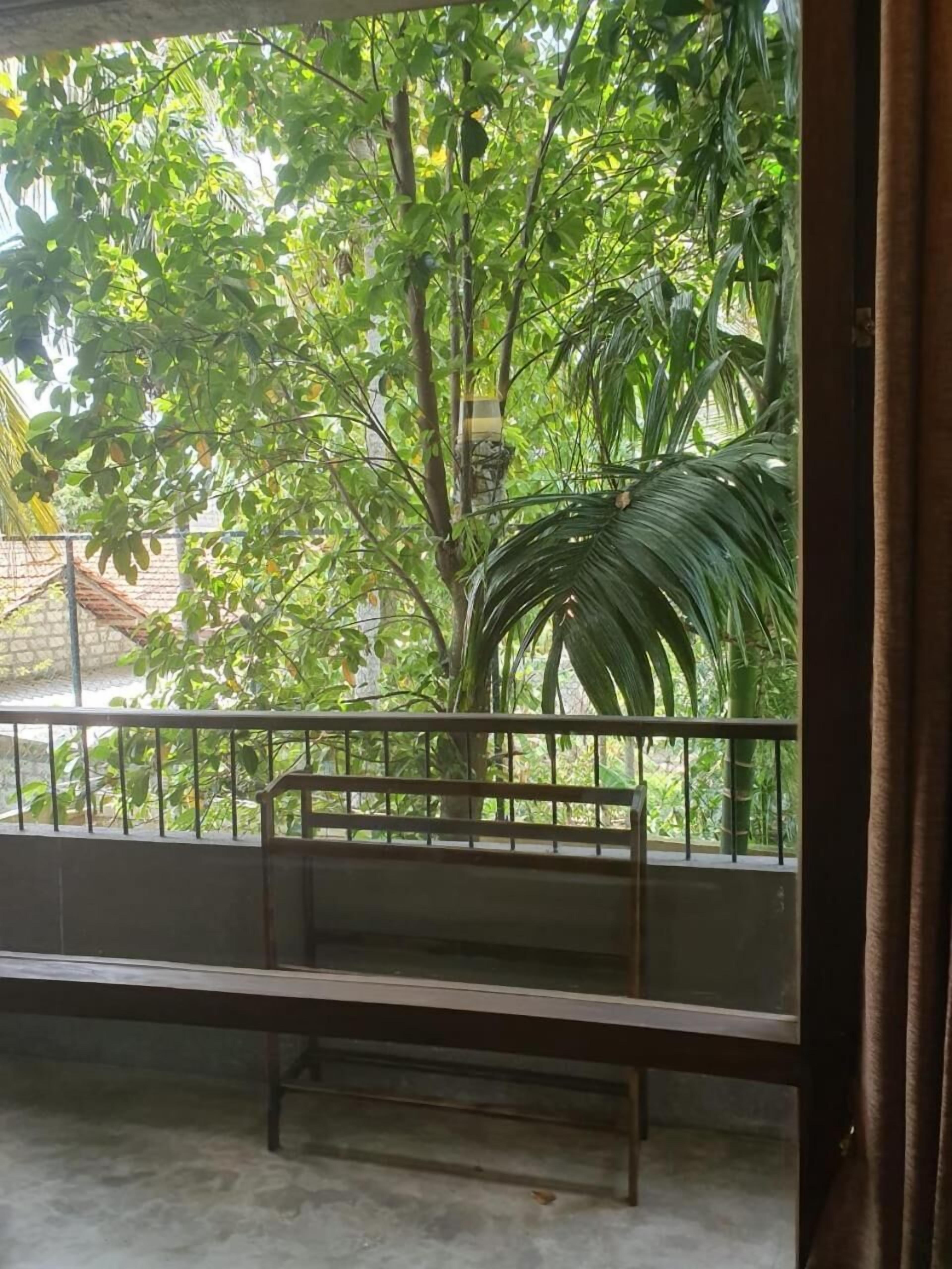 A balcony with a metal railing, a bench, and lush green foliage in the background.