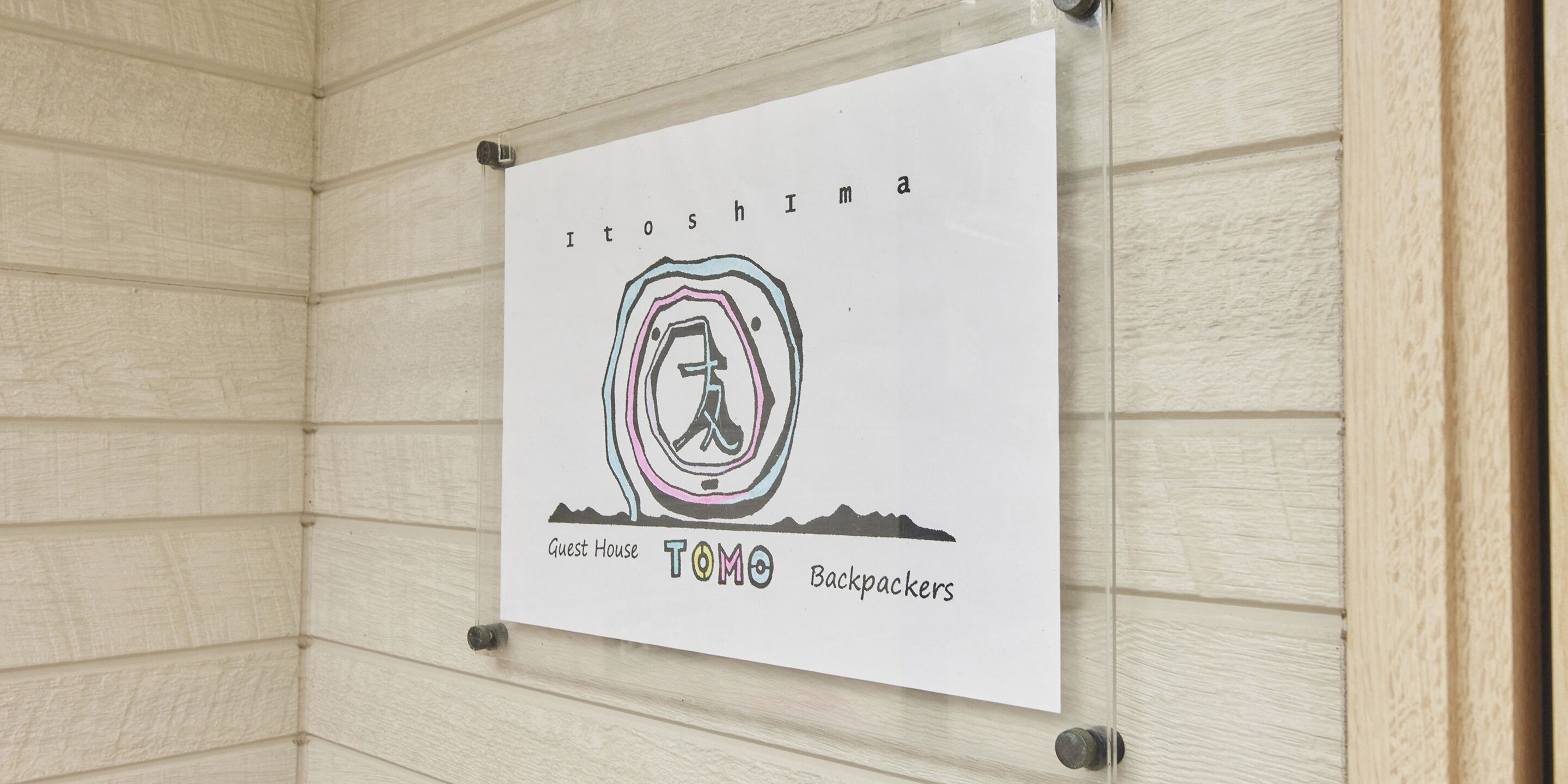Placa na parede com o texto 'Itoshima Guest House TOMO Backpackers'.