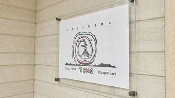 Placa na parede com o texto 'Itoshima Guest House TOMO Backpackers'.