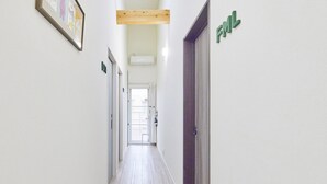 Un pasillo con una viga de techo de madera, un cuadro enmarcado a la izquierda y una puerta con un cartel verde a la derecha.